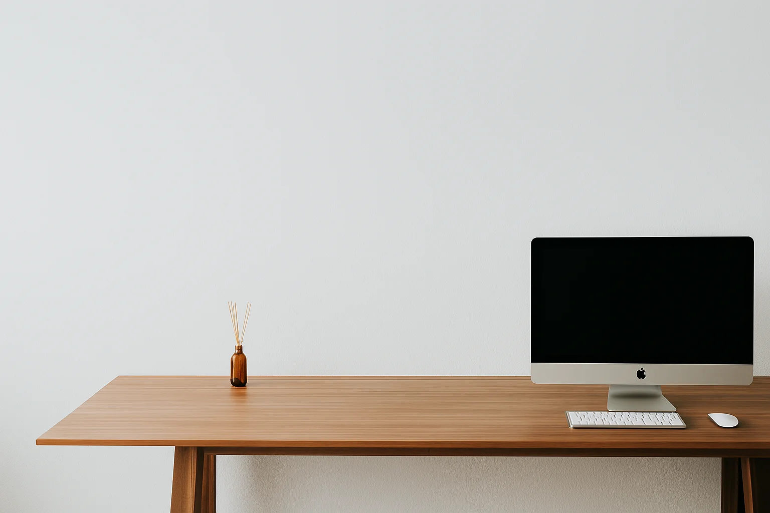 Minimalist workspace with a wooden desk, and an iMac computer, and a small reed diffuser.